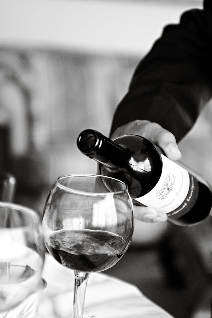 A classic black and white photograph of a wine being poured into a glass, capturing elegance in an Italian setting.