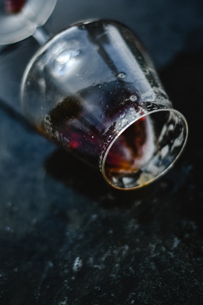 A detailed shot of a tipped glass with remnants of liquid on a textured dark background.