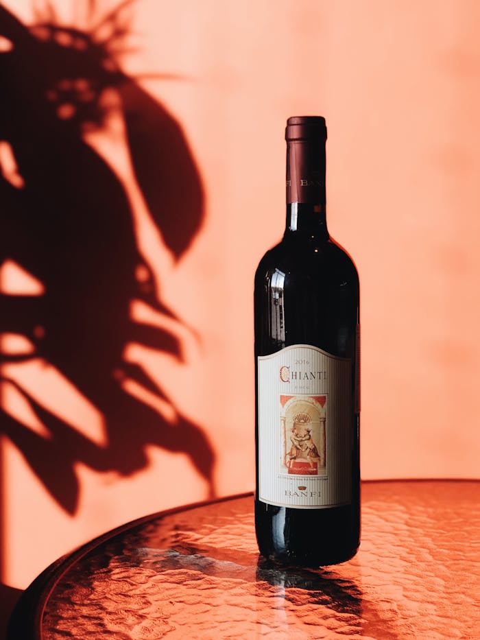 A bottle of Chianti wine on a glass table with artistic shadows and warm tones.