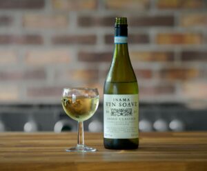 A bottle of Inama Vin Soave wine alongside a filled glass on a wooden table.
