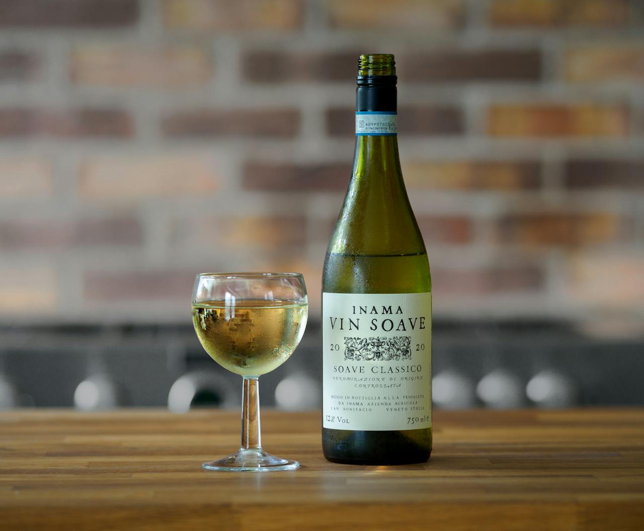 A bottle of Inama Vin Soave wine alongside a filled glass on a wooden table.